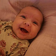 Sylvia is registered to the contest to win money with this photo: baby, smiling, face, infant, cushion, pink, floral, clothing, happy, portrait, child, young, cute, head, closeup, lying, soft, comfort, indoors, person