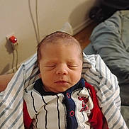 Giovanni is registered to the contest to win money with this photo: newborn, baby, sleeping, face, blanket, clothing, indoor, person, infant, cute, resting, young_child, striped, onesie, red, navy, soft_light, cozy, peaceful, portrait
