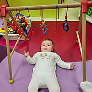 Axel a rejoint le concours — aidez-le/la à gagner de superbes lots ! baby, baby_gym, child, childcare, colorful, cute, early_childhood, floor_mat, hanging_toys, indoor, infant, lying_down, onesie, padded_floor, person, playroom, playtime, red_hair, toys, wooden_toys