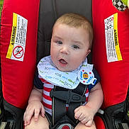 Bailor joined the competition — help win amazing prizes! baby, infant, car_seat, red, striped_clothing, bib, sitting, child, cute, face, expression, safety_harness, plush_toy, outdoor, grass, bright_colors, young_child, portrait, clothing, hand