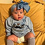 baby, child, blue_bow, headband, blue_sweater, cartoon_design, mustard_couch, yellow_couch, sitting, knee_high_socks, chubby_legs, wide_eyes, indoors, cute, infant, portrait, clothing, expression, person, comfortable