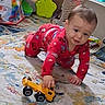 baby, child, crawling, toy_truck, red_pajamas, playroom, rug, indoor, portrait, face, hands, smiling, infant, toys, colorful, floor, baby_gear, home, sitting, playtime