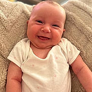 Margot joined the competition — help win amazing prizes! baby, smiling, infant, onesie, blanket, cute, face, skin, chubby_cheeks, happy, portrait, child, soft_texture, cozy, indoors, person, newborn, relaxed, young_child, warm_lighting