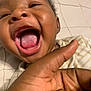 Liam is registered to the contest to win money with this photo: baby, close_up, mouth_open, hand, laughing, joyful, infant, skin, face, expression, blanket, bed, striped_clothing, cute, child, portrait, happy, playful, indoor, person