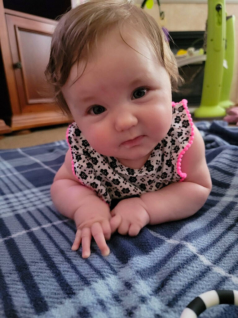 Coraline is registered to the contest to win money with this photo: baby, baby_toddler_clothing, cheek, child, door, dress, face, floor, flooring, hardwood, head, iris, nose, pattern, person, skin, sleeve, smile, thumb, toddler