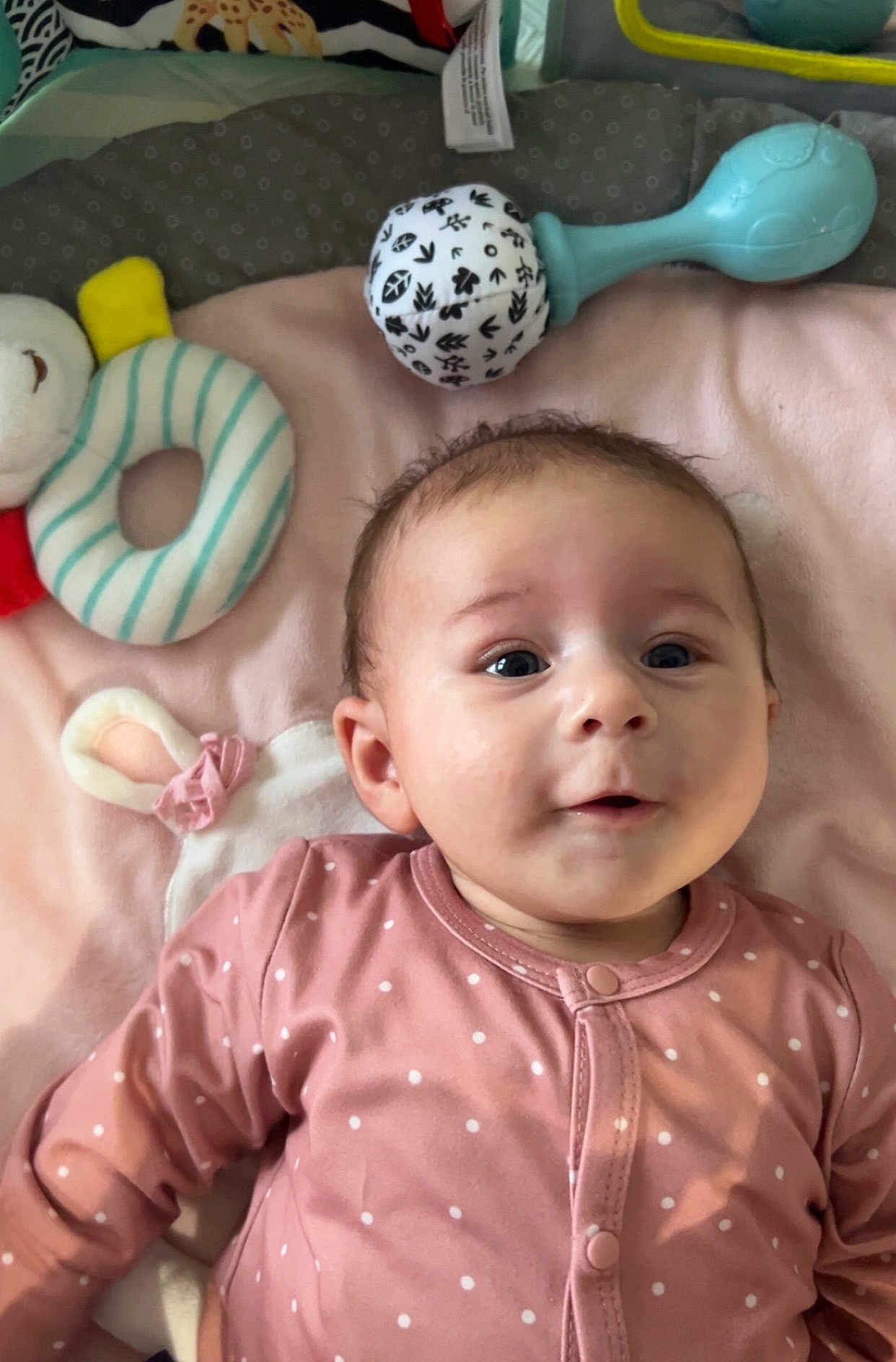 Adèle a rejoint le concours — aidez-le/la à gagner de superbes lots ! baby, infant, child, smiling, onesie, polka_dot, toy, rattle, play_mat, blanket, lying_down, face, eyes, cheeks, mouth, ear, hair, adorable, indoor, soft_toy