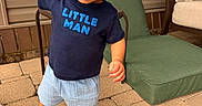 Benjamin is registered to the contest to win money with this photo: child, toddler, curly_hair, standing, outdoor, patio, smiling, portrait, blue_shirt, text_on_clothing, shorts, sneakers, adult_hand, chair, cushion, brick_pavers, playful, family, daylight, home
