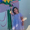child, girl, flower, bouquet, mural, wall, painting, dress, sandals, outdoor, sunlight, smile, happy, standing, concrete, colorful, young, nature, art, portrait