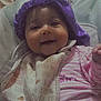 Dezeriah Sparks is registered to the contest to win money with this photo: baby, infant, smiling, purple_bonnet, bib, striped_clothing, seated, indoor, bed, blanket, face, happy, child, person, cute, portrait, clothing, headwear, cozy, home