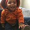 baby, child, infant, smiling, happy, portrait, orange_jacket, sun_hat, winter_clothing, shoe, sitting, couch, indoors, face, person, outdoor_style, cozy, fashion, playful, closeup