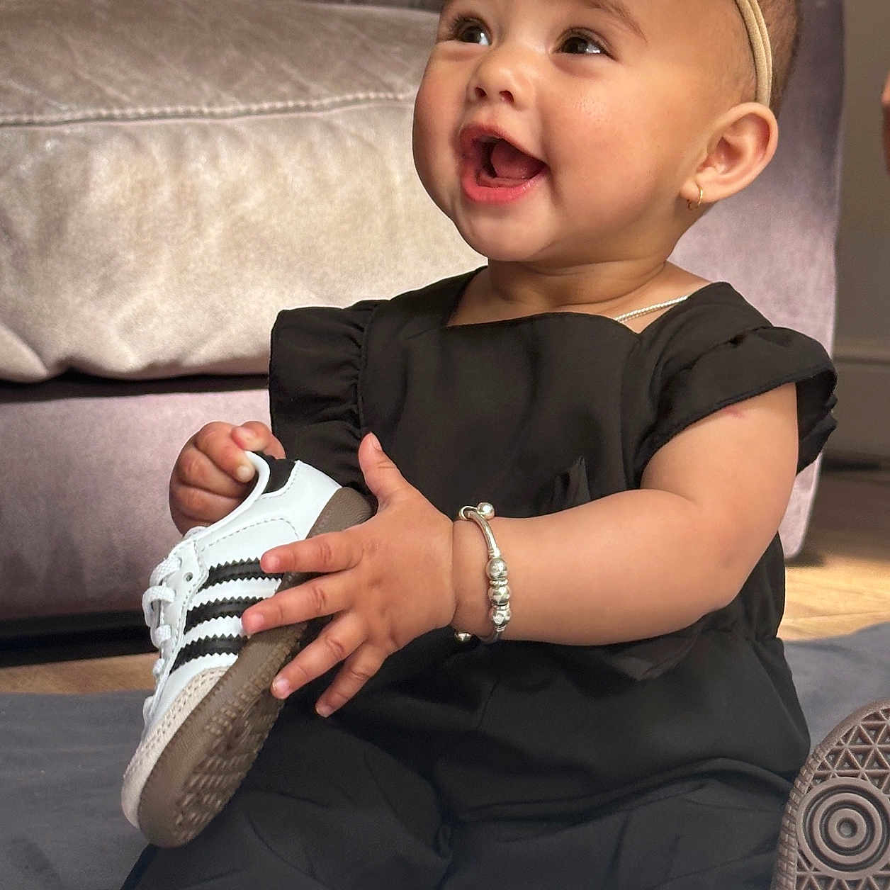 Maisha joined the competition — help win amazing prizes! accessory, baby, black_clothing, bracelet, child, couch, cute, fashion, floor, footwear, happy, headband, indoor, infant, person, portrait, sitting, smiling, sneaker, soft_light