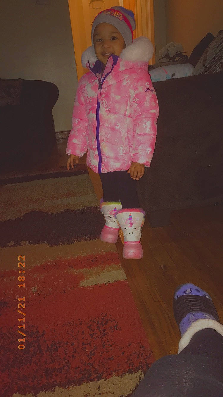 Isabella is registered to the contest to win money with this photo: baby, baby_products, baby_toddler_clothing, boot, carpet, cross_training_shoe, floor, flooring, headwear, hood, jacket, nightwear, outdoor_shoe, person, pink, plush, running_shoe, shoe, sock, stuffed_toy