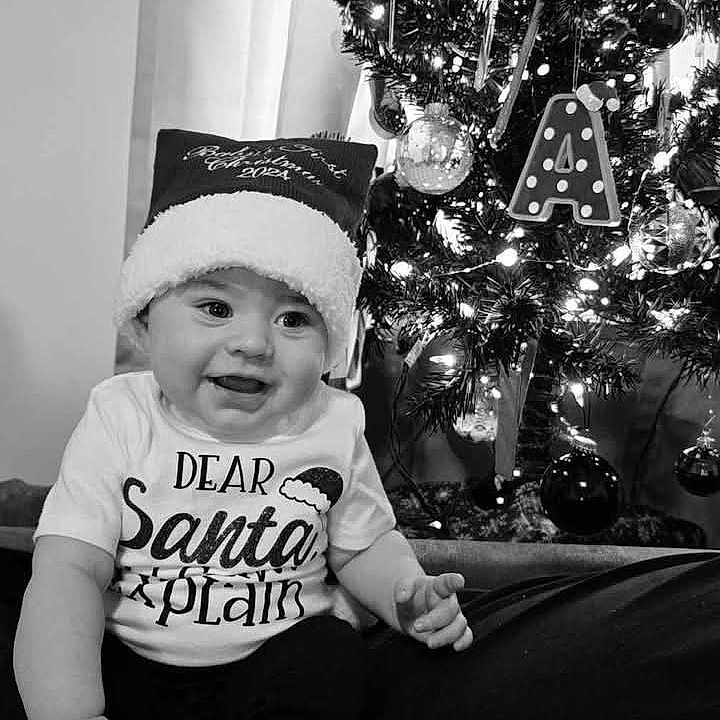 Ahari is registered to the contest to win money with this photo: baby, black_and_white, celebration, child, christmas, christmas_tree, cute, decoration, festive, happy, holiday, indoor, infant, lights, ornaments, portrait, santa_hat, seasonal, smiling, tshirt