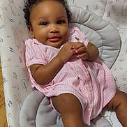 Kialsy is registered to the contest to win money with this photo: baby, child, infant, portrait, smiling, happy, sitting, pink_outfit, hair_bow, curly_hair, dark_skin, face, arms, legs, baby_seat, cushion, bunny_pattern, indoor, wood_floor, photography