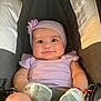 Rosita is registered to the contest to win money with this photo: baby, infant, child, car_seat, headband, flower, purple_clothing, mittens, smile, face, eyes, sitting, seatbelt, padded_seat, cute, adorable, young_child, indoor, person, portrait