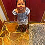 child, smiling, indoor, stone_floor, rug, door, red_door, sandals, shorts, striped_top, happy, person, portrait, floor, footwear, young_child, casual_clothing, standing, looking_up, playful