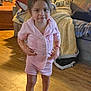 toddler, child, pajamas, pink_clothing, barefoot, wooden_floor, living_room, couch, blanket, pillow, indoor, person, furniture, home, curly_hair, expression, standing, cozy, casual, floor