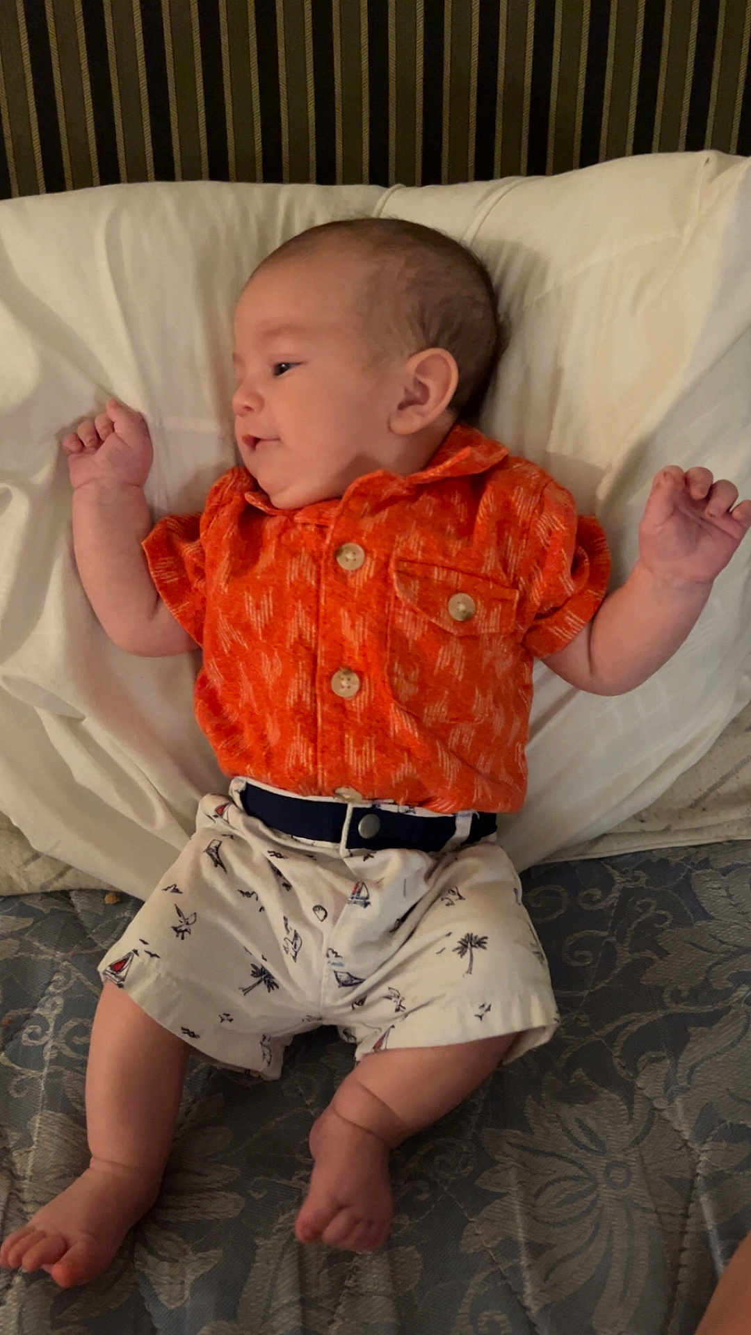 Johnathon Reinhardt is registered to the contest to win money with this photo: baby, infant, child, orange_shirt, shorts, bed, pillow, mattress, patterned, lying_down, cute, small, skin, face, hands, feet, clothing, indoor, relaxed, portrait