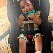 Maria joined the competition — help win amazing prizes! baby, child, car_seat, teething_toy, smiling, shoes, bows, clothing, sitting, indoor, floor, tile, straps, happy, person, cute, infant, chewing, play, secure