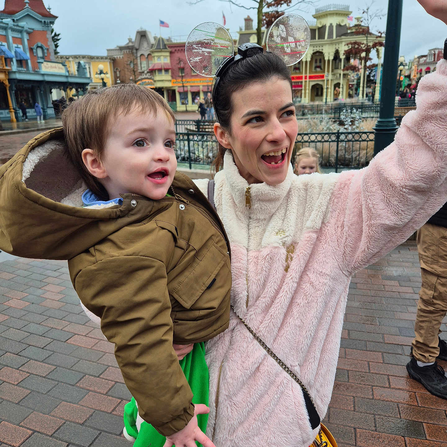 Link a rejoint le concours — aidez-le/la à gagner de superbes lots ! buildings, child, daytime, green_clothing, hand_raised, happy, jacket, mouse_ears, outdoor, pavement, people, polka_dots, portrait, red_skirt, smiling, theme_park, toddler, tree, winter_clothing, woman