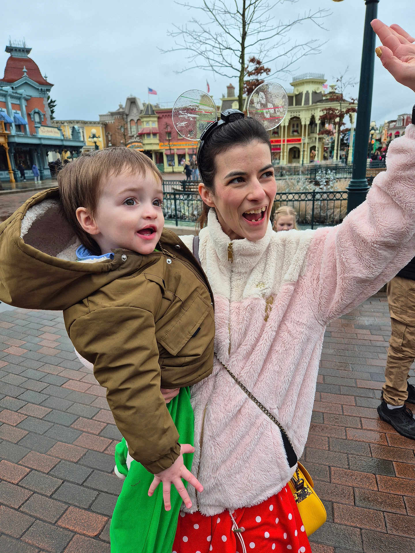 Link a rejoint le concours — aidez-le/la à gagner de superbes lots ! buildings, child, daytime, green_clothing, hand_raised, happy, jacket, mouse_ears, outdoor, pavement, people, polka_dots, portrait, red_skirt, smiling, theme_park, toddler, tree, winter_clothing, woman
