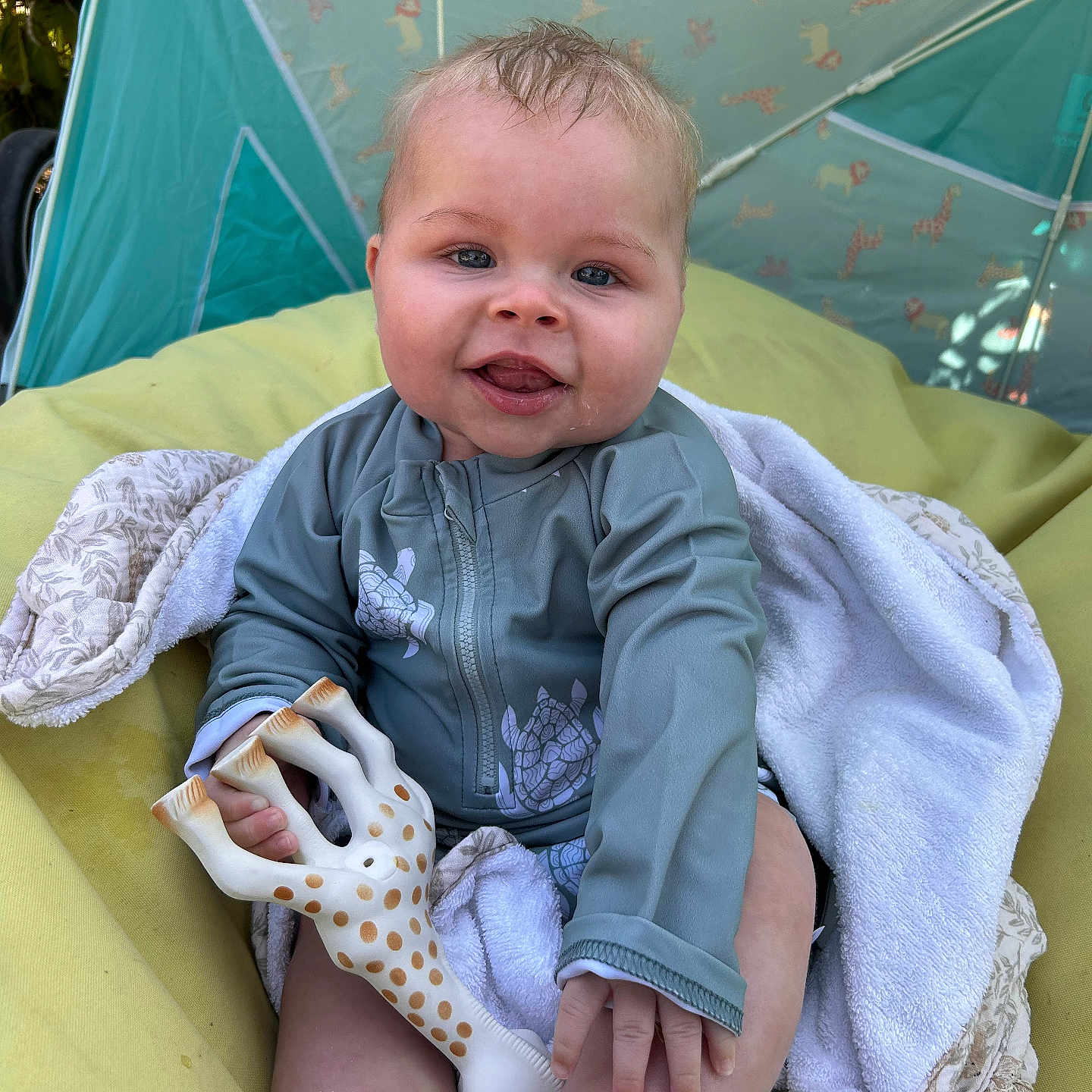 Noah participe au concours pour gagner de l'argent avec cette photo : baby, blanket, blue_clothing, child, cushion, cute, giraffe, happy, infant, nature, outdoor, person, playful, portrait, relaxing, smiling, sunlight, tent, toddler, toy