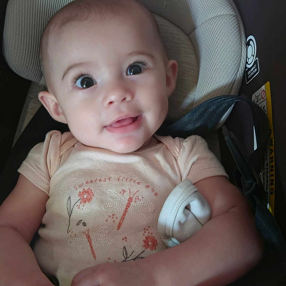 Sophia joined the competition — help win amazing prizes! baby, child, car_seat, onesie, smile, face, hands, legs, cushion, seat_belt, indoor, cute, infant, skin, person, apparel, head, eyes, expression, comfort