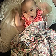 Sophia joined the competition — help win amazing prizes! baby, child, blanket, pillow, smiling, happy, face, arms, tongue, cute, infant, playful, indoors, fabric, patterned_blanket, person, portrait, soft_lighting, resting, young_child