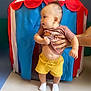 Monté a rejoint le concours — aidez-le/la à gagner de superbes lots ! baby, child, indoor, play_tent, colorful, yellow_shorts, brown_shirt, white_socks, curly_hair, mohawk, hand_holding, cute, infant, small_feet, standing, person, toy, playtime, support, expression