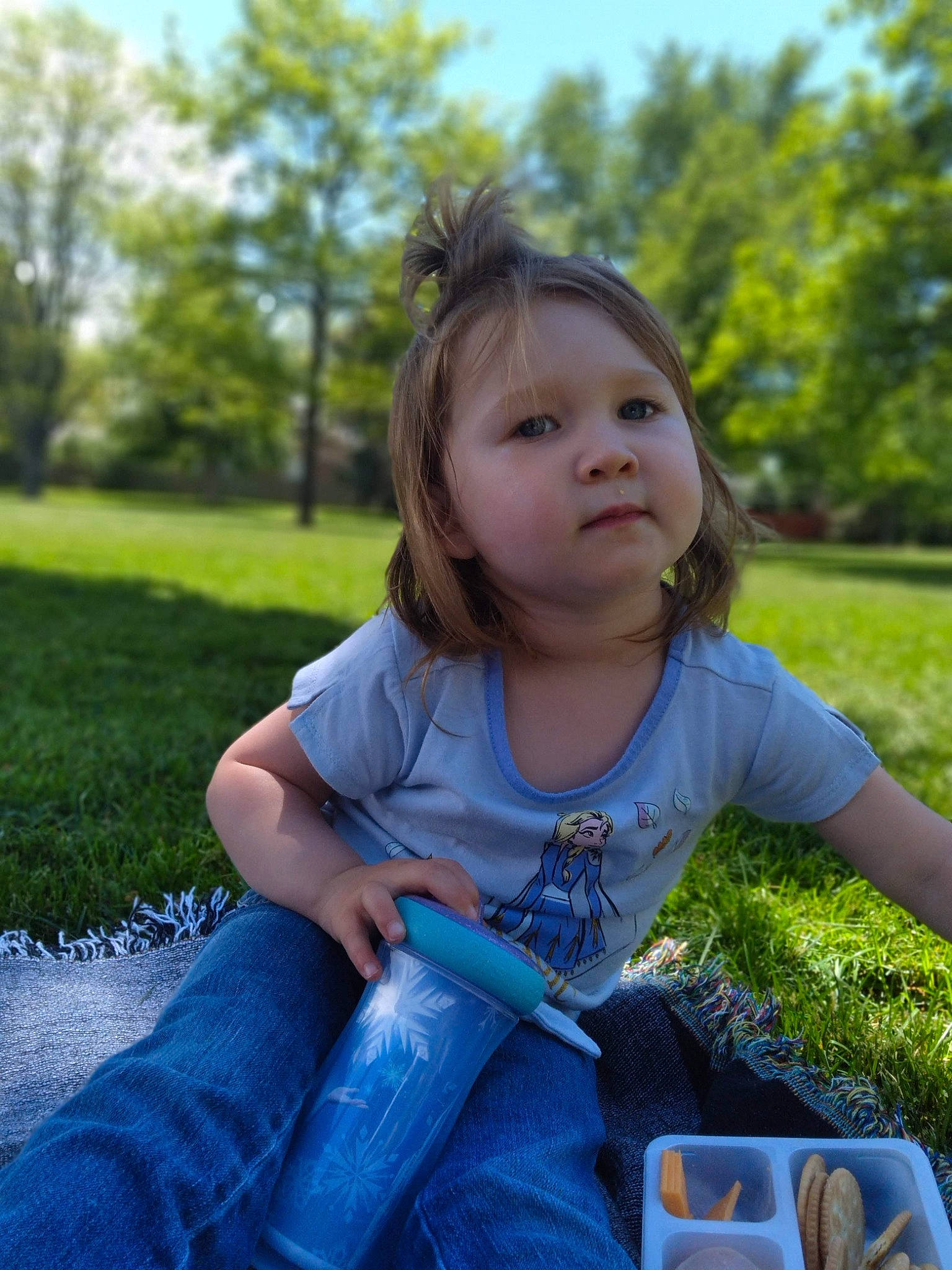 Ella is registered to the contest to win money with this photo: cup, drinkware, face, finger, fun, grass, green, happy, jeans, leaf, leisure, people_in_nature, person, plant, sky, summer, sunlight, tableware, toddler, tree