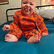 William joined the competition — help win amazing prizes! baby, bed, blue_bedspread, child, cute, foot, framed_picture, hand, head, indoor, infant, orange_clothing, person, playful, portrait, pumpkin_pattern, sitting, smiling, tongue_out, wall_art