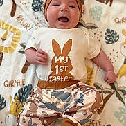 William is registered to the contest to win money with this photo: animal_hat, baby, blanket, child, cute, expression, face, foot, giraffe_pattern, happy, headwear, indoors, infant, leaf_pattern, lying_down, onesie, pants, playful, smiling, soft_texture
