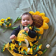 Alena participe au concours pour gagner de l'argent avec cette photo : baby, child, sunflower, plush, flower, yellow, black_clothing, blanket, smiling, cute, lying_down, decorative_flowers, soft_toys, portrait, indoors, infant, holding_object, happy, colorful, playful