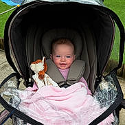 Francesca joined the competition — help win amazing prizes! baby, stroller, blanket, stuffed_animal, child, outdoor, smiling, happy, pink, face, seatbelt, protective_cover, grass, toy, infant, cute, person, head, clothing, safety