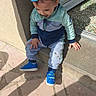 toddler, child, blue_cap, blue_shoes, sitting, doorstep, outdoor, sunlight, shadow, curious, casual_clothing, pavement, stone_floor, young_child, portrait, daylight, playful_shadows, person, jogging_suit, cap