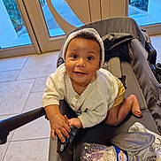 Marley participe au concours pour gagner de l'argent avec cette photo : baby, child, indoor, stroller, water_bottle, toy, clothing, sweater, hat, floor, tile, hand, foot, smile, face, curious, person, infant, cute, playful