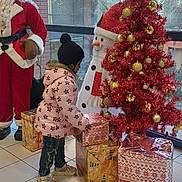 Boro Praise participe au concours pour gagner de l'argent avec cette photo : child, christmas_tree, presents, holiday_decorations, santa_claus, snowman, winter_clothing, pink_jacket, knit_hat, indoor, tiled_floor, festive, ornaments, window, seasonal, holiday, curious, jeans, sneakers, decorations