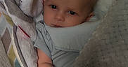 Zack joined the competition — help win amazing prizes! baby, infant, child, portrait, face, eyes_open, lying_down, blanket, pillow, bed, cozy, indoors, home, gray_clothing, stuffed_animal, soft_toy, textile, patterned_bedding, close_up, calm