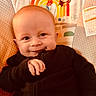 Zack is registered to the contest to win money with this photo: baby, child, infant, smiling, portrait, sitting, indoor, cozy, cushion, seat, black_clothing, patterned_background, rainbow, monkey, sun, colorful, happy, face, hands, photography