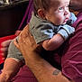 baby, infant, adult, arm, holding, grey_clothing, maroon_clothing, tattoo, indoor, closeup, person, skin, face, hand, couch, fabric, curious, newborn, human, portrait