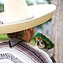 person, dog, sombrero, green_hat, poncho, face_paint, outdoor, blurred_background, pet, costume, small_dog, holding, animal, cute, expression, festival, celebration, human, portrait, hat