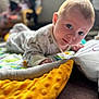 baby, infant, face, eyes, blanket, play_mat, clothing, hand, floor, indoors, soft_texture, curious, young_child, head, expression, home, child, person, couch, comfort