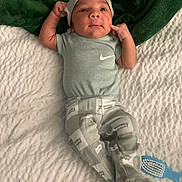 Rakai is registered to the contest to win money with this photo: baby, infant, clothing, blanket, green_blanket, blue_shirt, patterned_pants, face, expression, lying_down, baby_hat, baby_brush, white_blanket, curious, cute, small_hands, indoor, soft_texture, footwear, relaxed