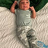 baby, infant, clothing, blanket, green_blanket, blue_shirt, patterned_pants, face, expression, lying_down, baby_hat, baby_brush, white_blanket, curious, cute, small_hands, indoor, soft_texture, footwear, relaxed