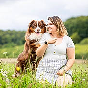 Horus a rejoint le concours — aidez-le/la à gagner de superbes lots ! dog, woman, grass, field, nature, smile, outdoor, pet, happy, animal, portrait, casual_clothing, watch, skirt, cloudy_sky, greenery, friendship, affection, sitting, daytime