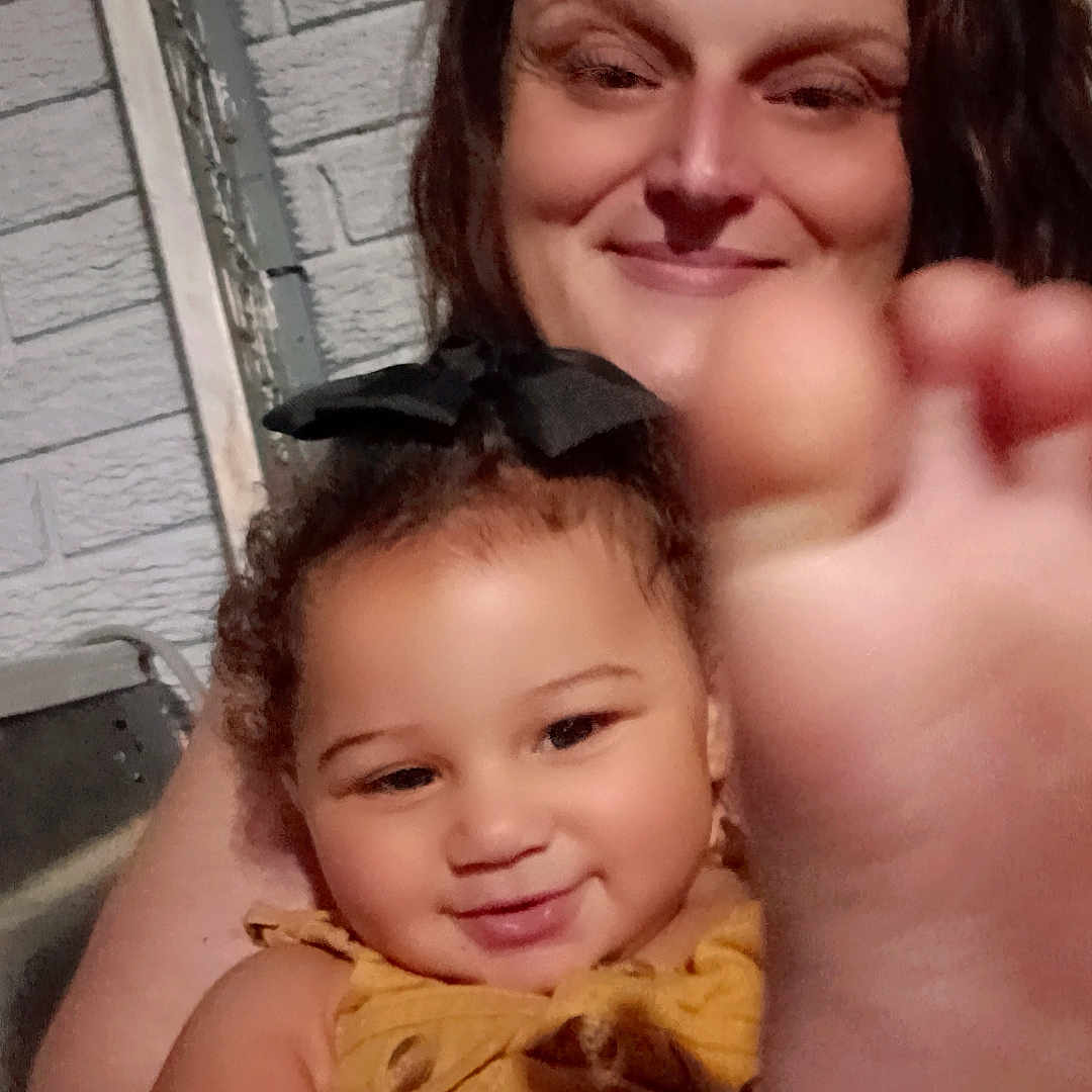 Angelise is registered to the contest to win money with this photo: arm, baby, bow, brick_wall, child, closeup, curly_hair, face, family, foot, hand, happy, holding, indoor, person, portrait, skin, smile, woman, yellow_clothing