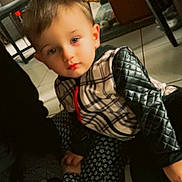 Maylon participe au concours pour gagner de l'argent avec cette photo : child, indoor, floor, person, jacket, patterned_clothing, hand, adult, furniture, tile_floor, quilted_sleeves, seated, young_child, holding_hands, casual, expression, brown_hair, home, cozy, soft_lighting