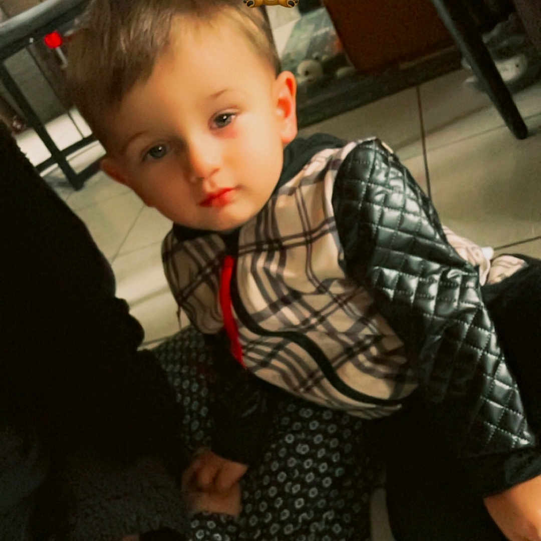 Maylon participe au concours pour gagner de l'argent avec cette photo : adult, brown_hair, casual, child, cozy, expression, floor, furniture, hand, holding_hands, home, indoor, jacket, patterned_clothing, person, quilted_sleeves, seated, soft_lighting, tile_floor, young_child