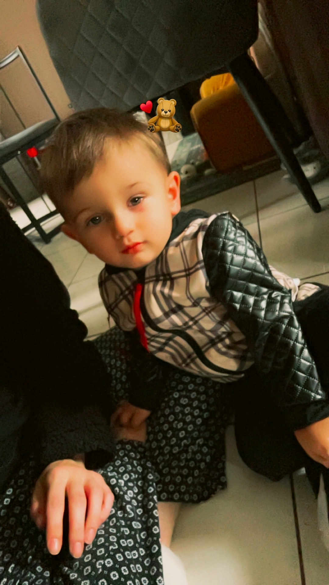 Maylon participe au concours pour gagner de l'argent avec cette photo : child, indoor, floor, person, jacket, patterned_clothing, hand, adult, furniture, tile_floor, quilted_sleeves, seated, young_child, holding_hands, casual, expression, brown_hair, home, cozy, soft_lighting