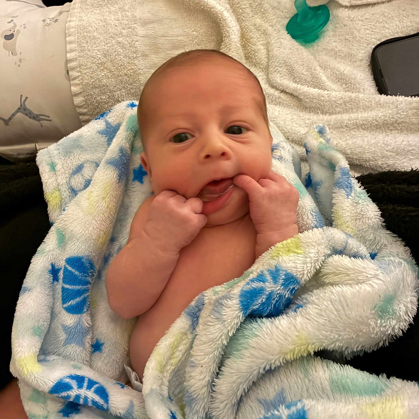 Tatum is registered to the contest to win money with this photo: baby, infant, child, portrait, face, smiling, eyes_open, hands, blanket, wrapped, cozy, indoor, lying_down, pacifier, phone, towel, soft_texture, close_up, adorable, family_photo